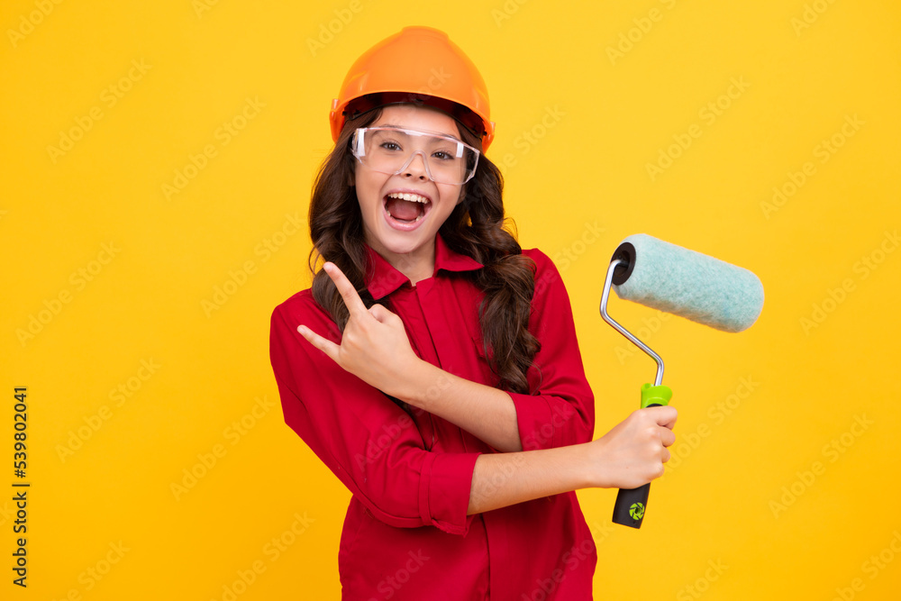 Teenager child painter in helmet with painting brush. Child in hard hat. Kid builder painter on construction site. Renovation and repair. Excited teenager girl. Teenager child painter in helmet with painting brush. Child in hard hat. Kid builder painter on construction site. Renovation and repair. Excited teenager girl.