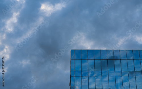 Sky reflection on the facade of a new modern glass and steel office corporation building.