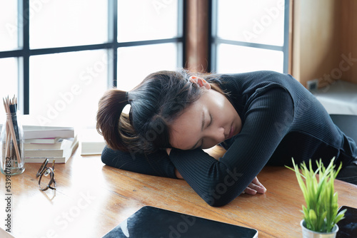 A portrait of a teenage Asian woman sleeping on a desk in the library due to fatigue from studying