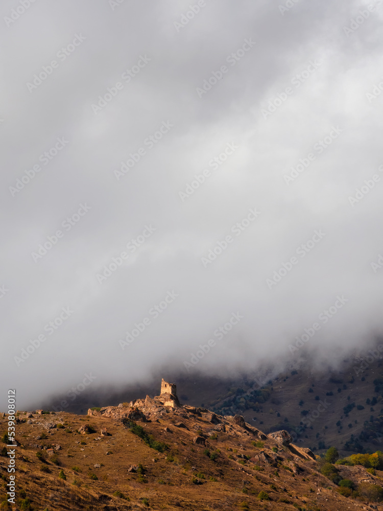Beautiful dramatic landscape nature view in the mountains. Old Ossetian battle tower in the misty mountains. Digoria region. North Ossetia, Russia. Vertical view.
