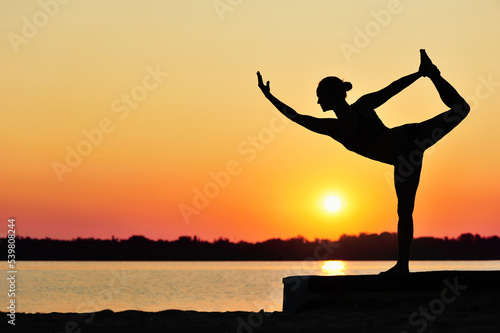 Silhouette of a yoga girl practicing one leg stand against the sunrise