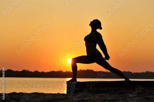 Sportive woman practicing warrior yoga pose at the beach