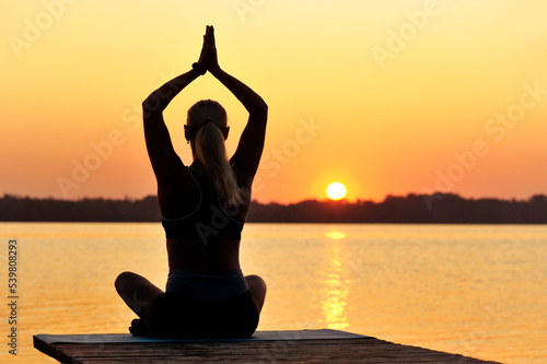 Silhouette of a meditating woman practicing yoga holding hands over head