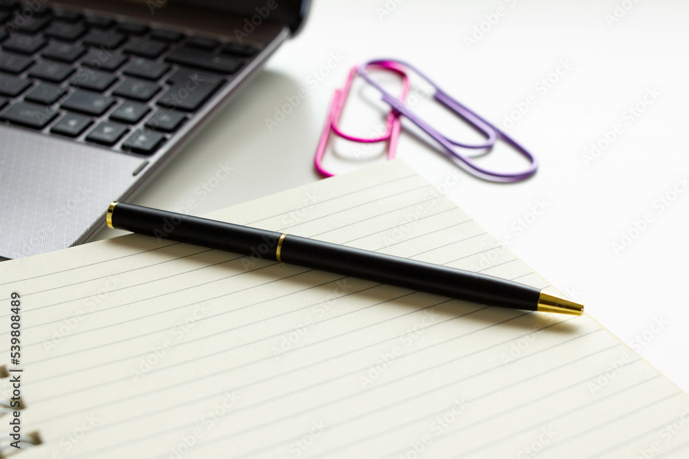 Blank notebook page for input text. Modern workspace on a white desk table with laptop, keyboard and other office supplies. Still life workplace view with copy space. Selective focus. Blank notebook page for input text. Modern workspace on a white desk table with laptop, keyboard and other office supplies. Still life workplace view with copy space. Selective focus.