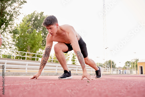 tattooed man starting to run on athletics track