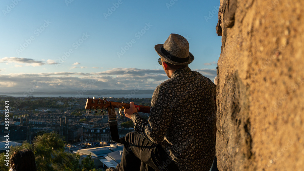 A Man with guitar overlooking Edinburgh landscape from Calton Hill