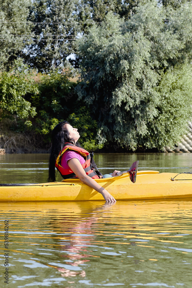 Confident middle aged woman relaxing in yellow kayak on summer river. Having fun in leisure activity. Kayaking, sport, relations concept. Confident middle aged woman relaxing in yellow kayak on summer river. Having fun in leisure activity. Kayaking, sport, relations concept.