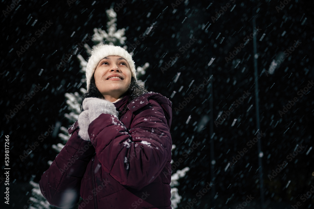Portrait of delightful beautiful woman in warm clothes, looking up to the sky, enjoying christmas atmosphere outdoors on snowy evening. Snowfall. Winter holidays and Merry Christmas concept Portrait of delightful beautiful woman in warm clothes, looking up to the sky, enjoying christmas atmosphere outdoors on snowy evening. Snowfall. Winter holidays and Merry Christmas concept