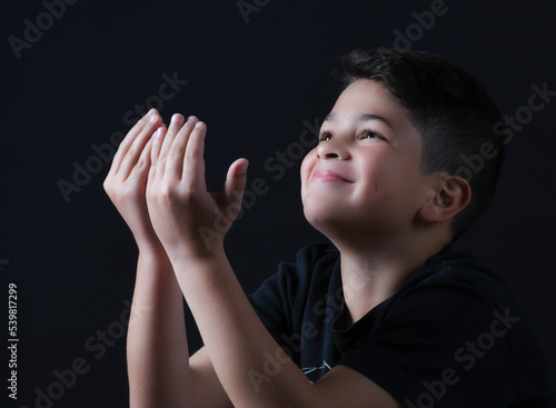 cute boy posing and smiling in a photography studio with a black T-shirt and black background 
