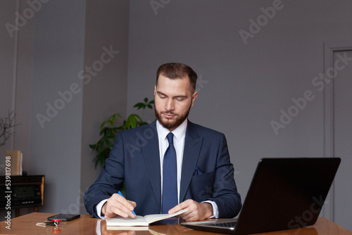 Confident businessman in suit is writing notes while working. Multi-tasking concept