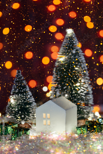 Christmas cute little house with tree in snow. Glowing festive garland on dark background. Cozy atmosphere with home decor with selective focus. New Year card © Alex Shi