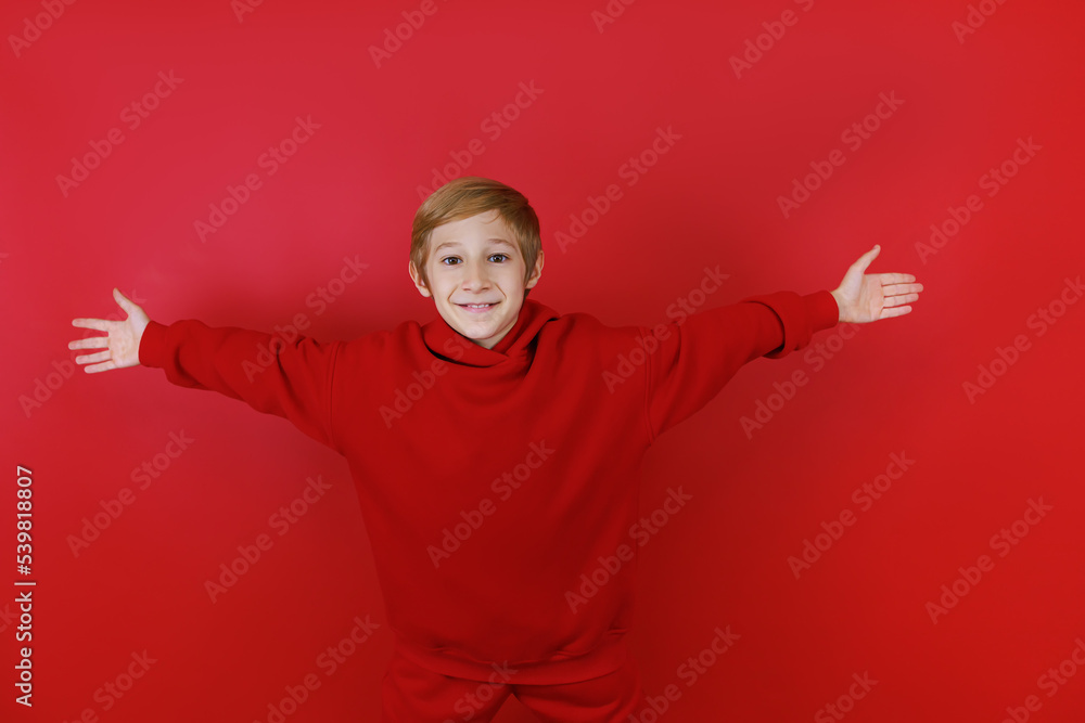 Cheerful boy on a red background and dressed in a red suit stretched out his arms to the sides Cheerful boy on a red background and dressed in a red suit stretched out his arms to the sides