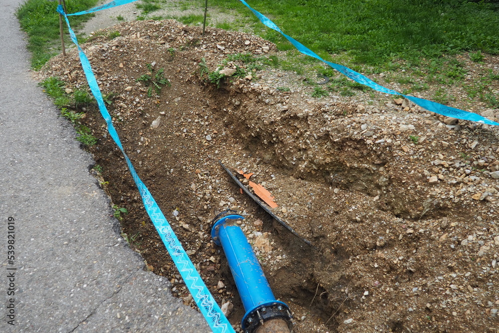 Broken ground, hole. Blue water pipes. Repair of the city water supply network. The inscription in Serbian - attention, plumbing. Earthworks of municipal services. Depreciation and amortization