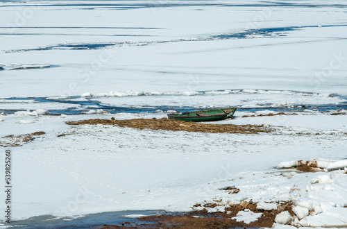 Old boat in a partially frozen lake. The boat is covered with snow