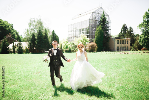 Newly married couple running and jumping in park while holding hands