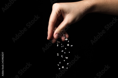 Coarse rock salt on a black background. Hand pours coarse salt