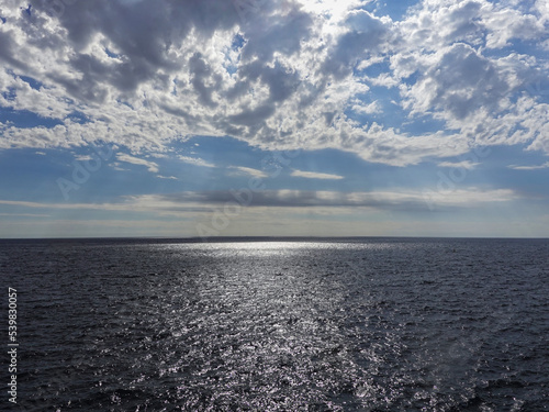 Reflections of the sun in the grey mediterranean sea. Blue sky with big grey clouds. 
