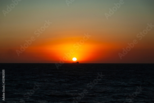 Sunset at sea and the silhouette of a transport ship in the distance on the horizon under the sun. © Сергей Жмурчак