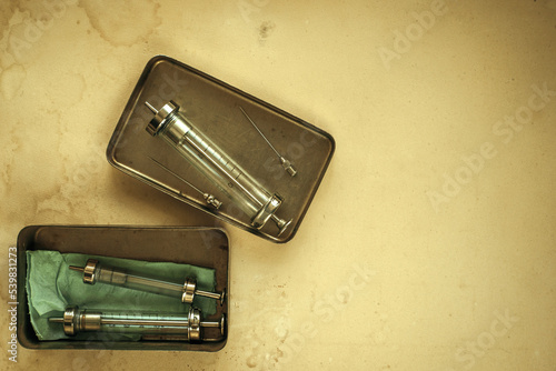 Glass syringes in metal containers on old paper. Reusable syringe of the last century.Problems of drug addiction. Vintage picture with syringes and needles has been on the table for centuries. photo