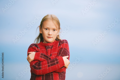 Outdoor portrait of beautiful little girl wearing red sweater, showing cold sign