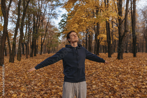 Carefree man enjoying freedom in nature with closed eyes while standing in autumn park among trees  © Dzmitry