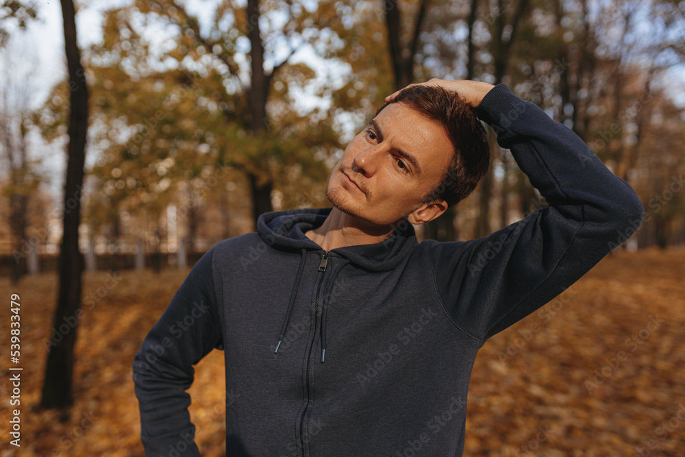 Sporty male athlete stretching neck and doing warm up while exercising during fitness training in park in autumn Sporty male athlete stretching neck and doing warm up while exercising during fitness training in park in autumn