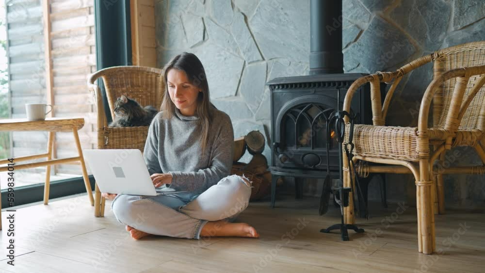 Woman using laptop while sitting near the fireplace in cozy interior. Woman using laptop while sitting near the fireplace in cozy interior.