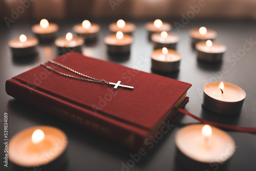 Silver christian cross on red paper bible book on table over burning candles close up photo