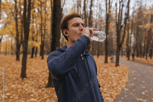Concentrated sportsman drinking water during workout break in autumn park