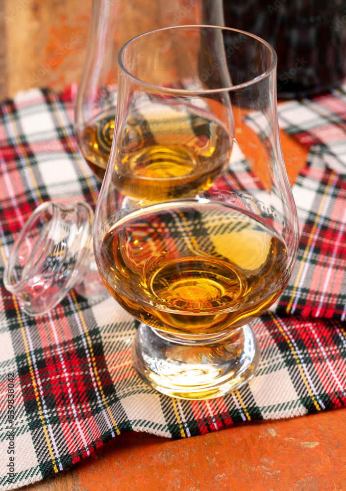 Tulip-shaped tasting glass with dram of Scotch single malt or blended whisky on wooden table with tartan Tulip-shaped tasting glass with dram of Scotch single malt or blended whisky on wooden table with tartan