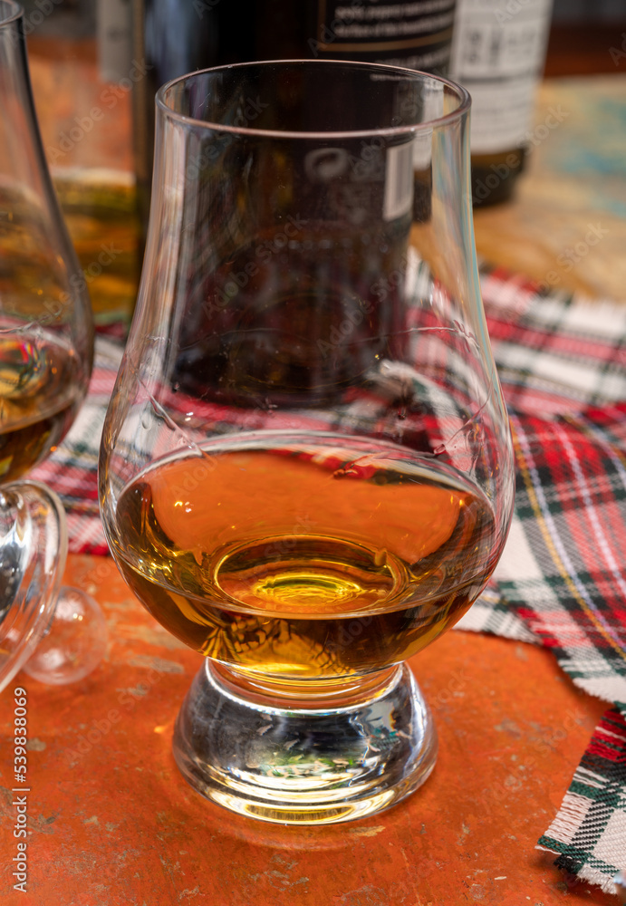 Tulip-shaped tasting glass with dram of Scotch single malt or blended whisky on wooden table with tartan Tulip-shaped tasting glass with dram of Scotch single malt or blended whisky on wooden table with tartan