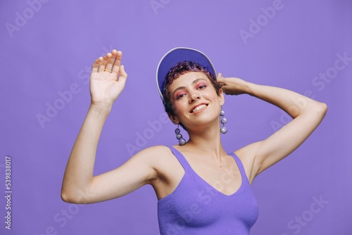 Sports fashion woman dancing posing smiling with teeth in a purple sports suit for yoga on a slender body and a transparent cap on her head on a purple background monochrome