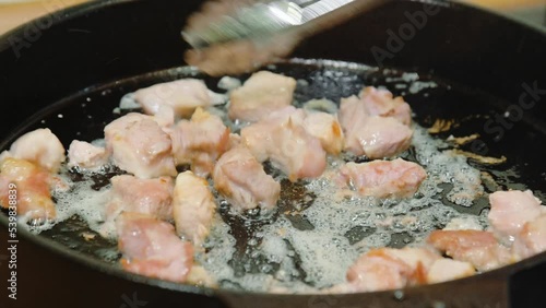 The cook stirs meat with culinary tongs, which is fried in boiling olive oil in a cast-iron frying pan