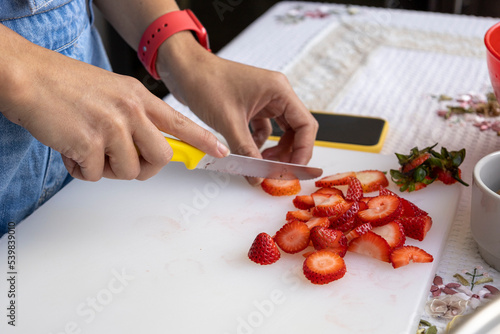 cutting strawberries into pieces with a knife, food preparation for dessert, fresh fruit, hobbies and lifestyle in the kitchen