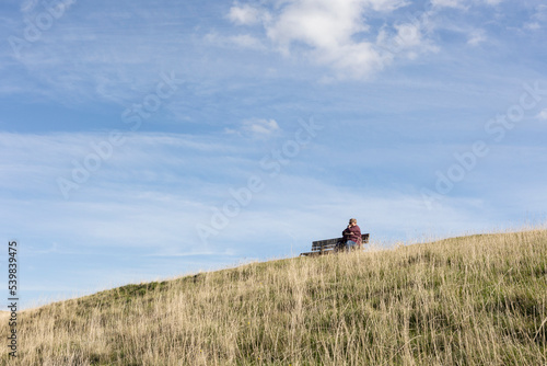 woman sitting alone on a bench deep in thought under blue summer skys, copy space, solitude concept