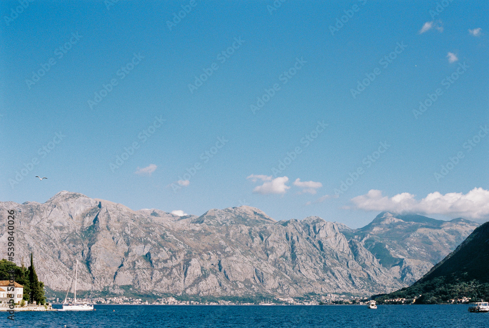 Boats float on the sea off the coast of Perast against the backdrop of a mountain range