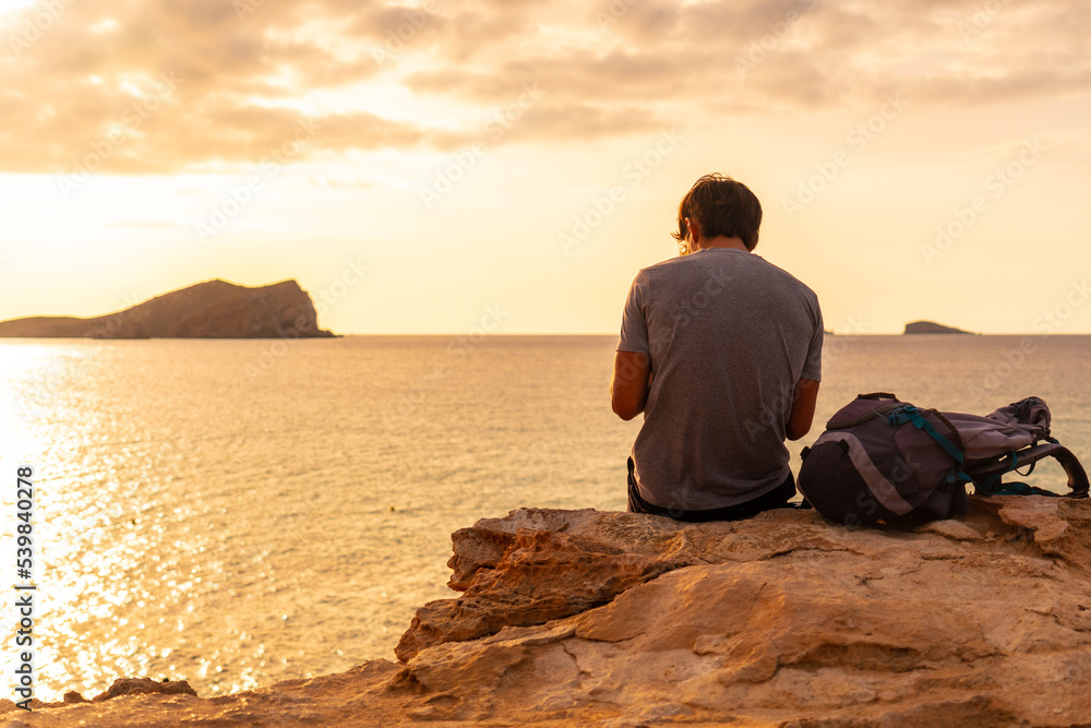 A tourist sitting watching the sunset at Cala Comte beach on the island of Ibiza. Balearic