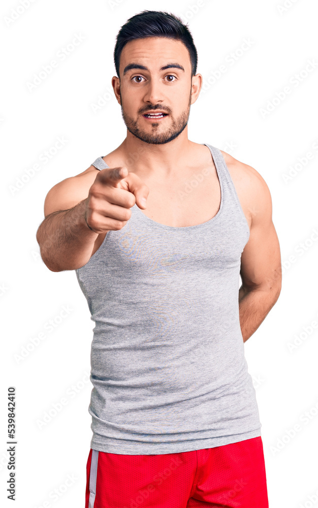Young handsome man wearing swimwear and sleeveless t-shirt pointing displeased and frustrated to the camera, angry and furious with you Young handsome man wearing swimwear and sleeveless t-shirt pointing displeased and frustrated to the camera, angry and furious with you