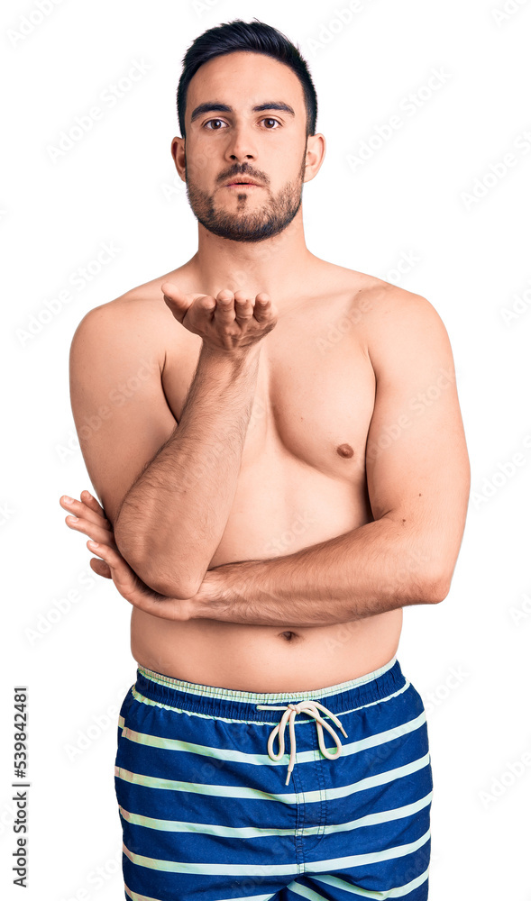 Fototapeta premium Young handsome man wearing swimwear looking at the camera blowing a kiss with hand on air being lovely and sexy. love expression.