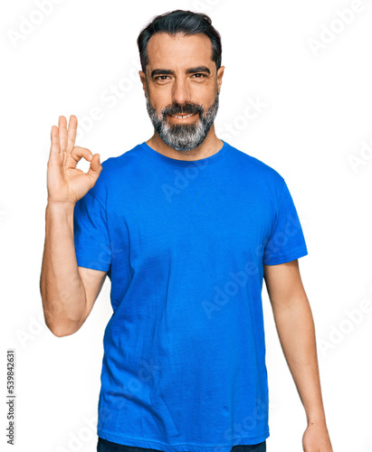 Middle aged man with beard wearing casual blue t shirt smiling positive doing ok sign with hand and fingers. successful expression.