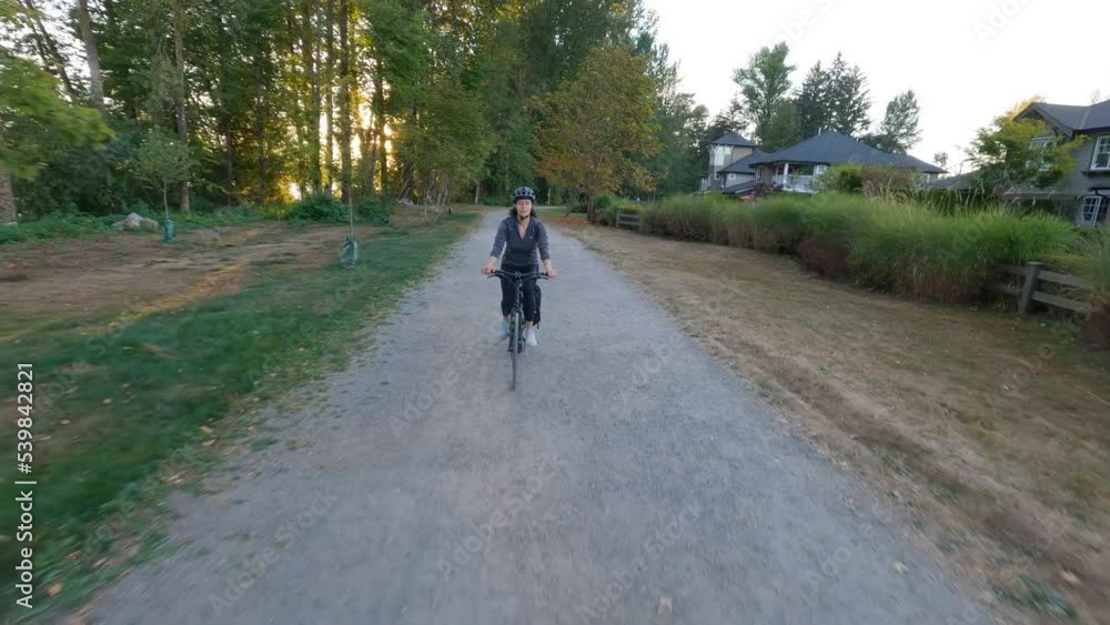 Adventure Woman bike riding on a bicycle trail surrounded by green trees. Summer Sunset. Pitt Meadows, Greater Vancouver, British Columbia, Canada. Adventure Woman bike riding on a bicycle trail surrounded by green trees. Summer Sunset. Pitt Meadows, Greater Vancouver, British Columbia, Canada.