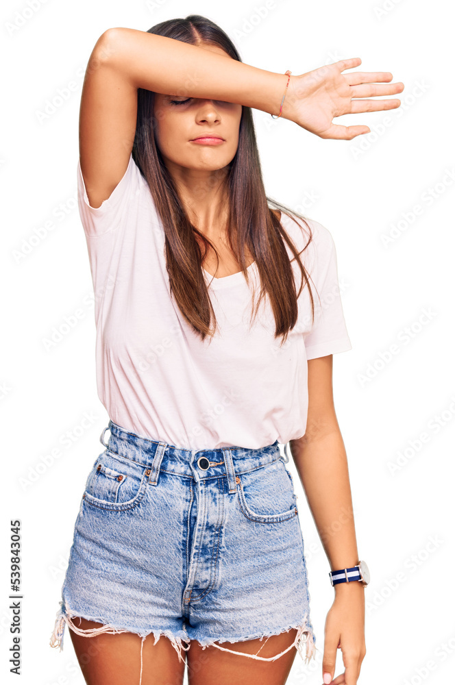 Obraz premium Young hispanic woman wearing casual white tshirt covering eyes with arm, looking serious and sad. sightless, hiding and rejection concept