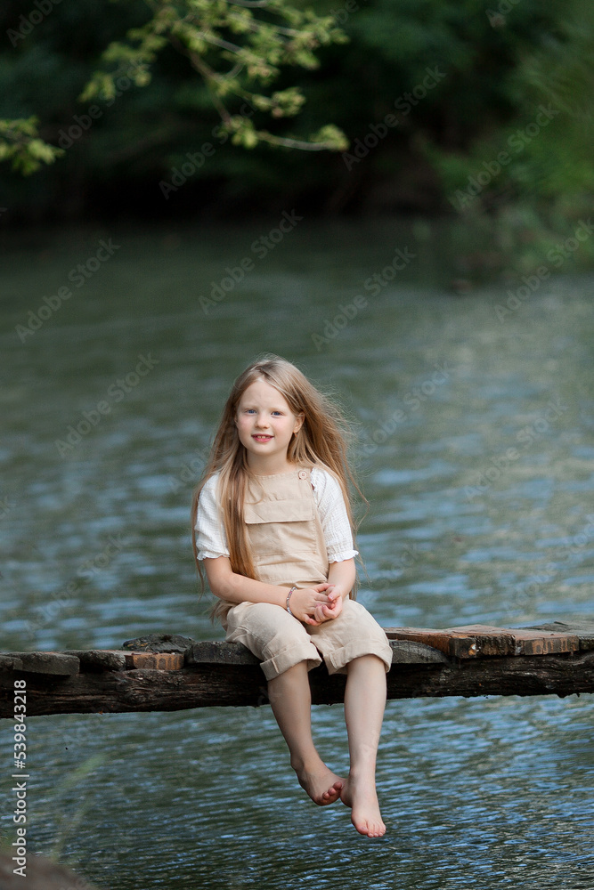 children walk on the bridge across the river fishing with a stick play in summer in overalls children walk on the bridge across the river fishing with a stick play in summer in overalls