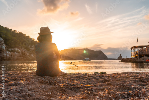 A young woman sitting looking at Benirras beach in Ibiza at sunset. vacation concept photo