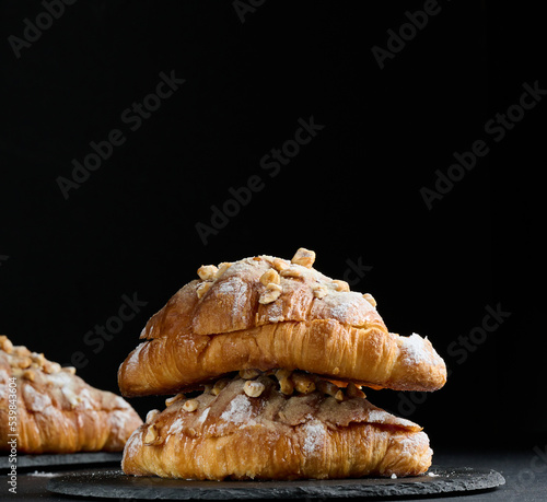 Baked croissant on a  board and sprinkled with powdered sugar, black table. Appetizing pastries for breakfast.