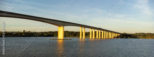 Low-angle of a sunlit Orwell bridge at sunset, a cloudy sky and cityscape background