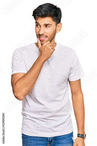Young handsome man wearing casual white tshirt with hand on chin thinking about question, pensive expression. smiling with thoughtful face. doubt concept.