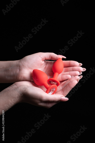Two red anal plugs in female hands on a black isolated background. Sex toys for ass. Copy space for text