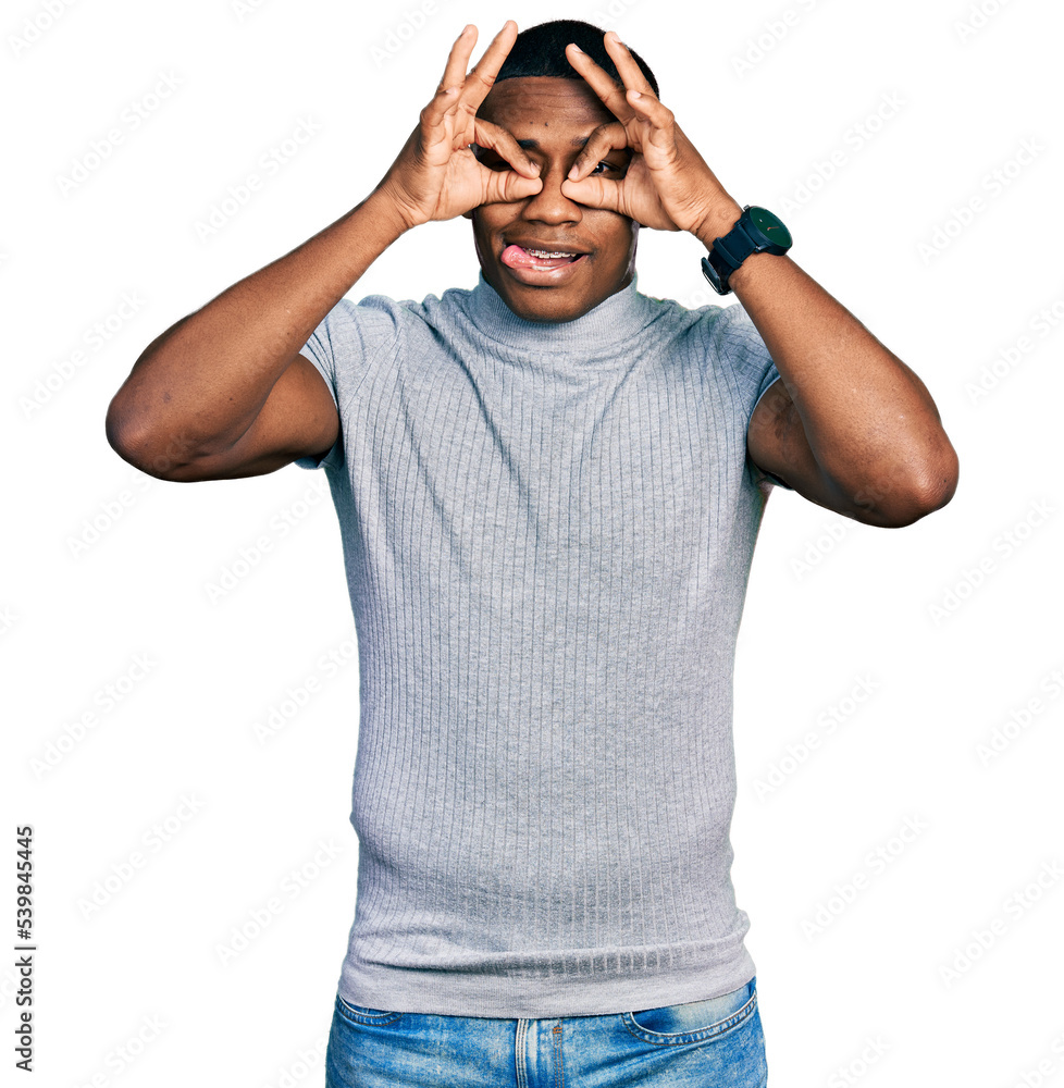 Young black man wearing casual t shirt doing ok gesture like binoculars sticking tongue out, eyes looking through fingers. crazy expression. Young black man wearing casual t shirt doing ok gesture like binoculars sticking tongue out, eyes looking through fingers. crazy expression.
