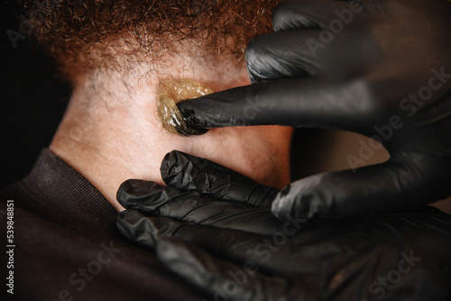 Sugaring master removes beard hair to a white man with sugar paste